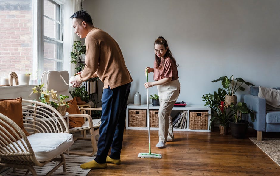 A cheerful couple cleaning their living room together, surrounded by indoor plants and cozy furniture.